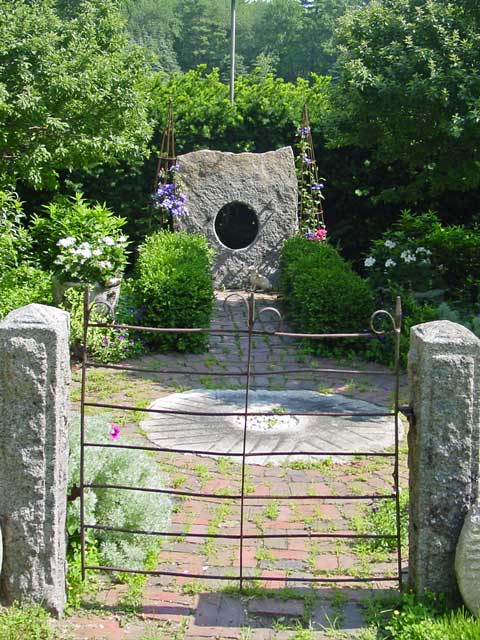 an iron gate leads into a secret garden with stone wheel and cut out features